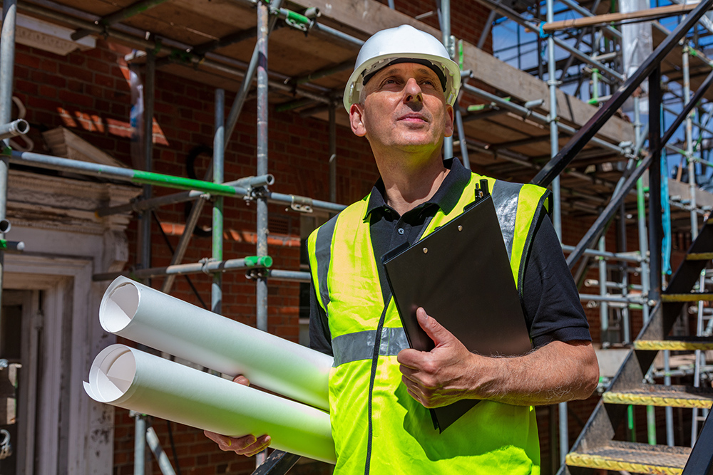 Man in high vis top with clip board and plans on building site