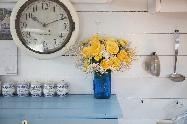 Rustic shabby chic kitchen with wall clock and yellow flowers in a blue vase