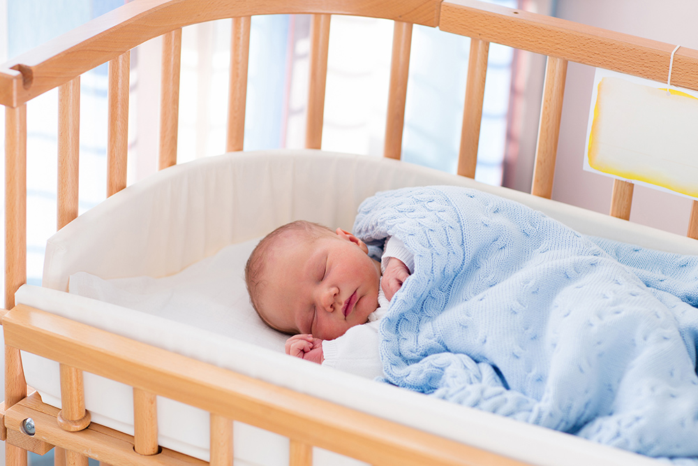 Baby sleeping in wooden cot with blue blanket