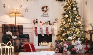 Christmassy living room with arm chair next to the fireplace full of candels. Mantelpiece covered in Christmas ornaments and toys, and stockings hanging over the fire place. Large decorated Christmas tree covered in lights and surrounded by presents