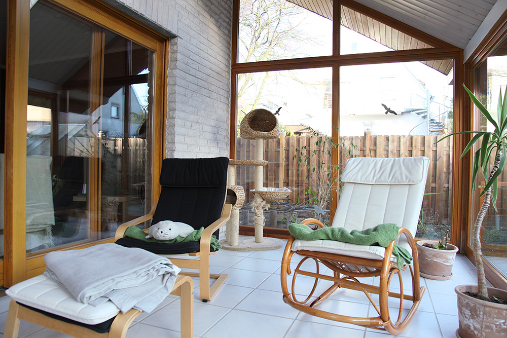 Black and white ikea poang chair in large conservatory with tiled flooring and cat tree.