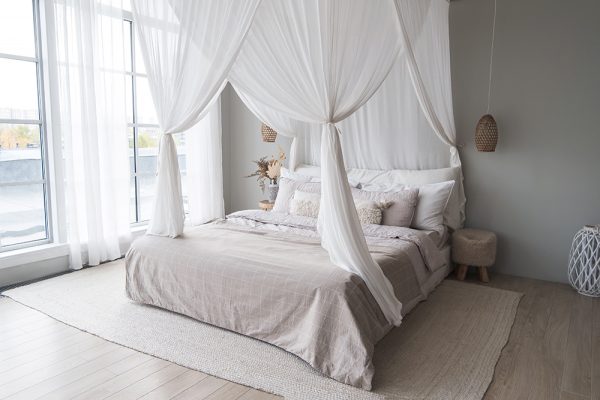 Bedroom with muted tones. Four poster bed with draps, large jute rug positioned under the bed and large windows