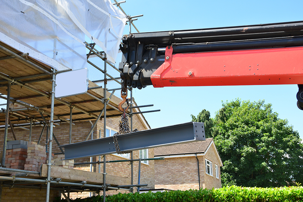 A crane lifting a girder into position on building site. House extention being built