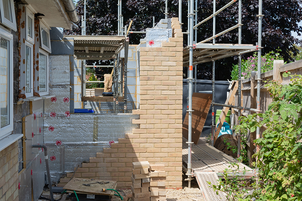 Renovation projects. Building of extension of the existing house, unfinished brick walls, block work, insulation, stacks of materials on scaffoliding