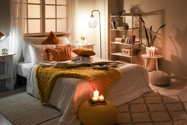 Bedroom with mustard colour throw, orange pillows and mood lighting with lamps and candles