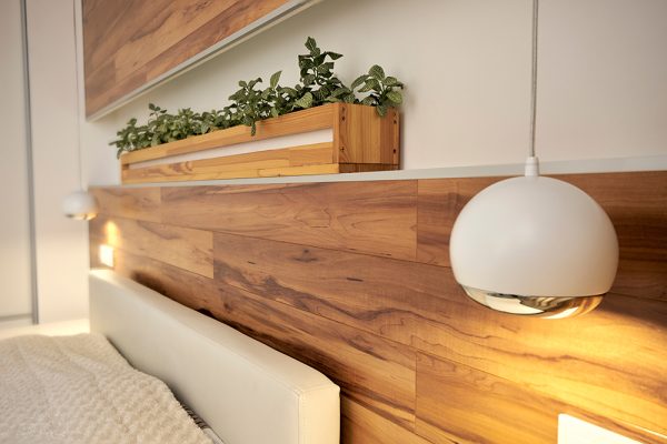 Bed with wooden headboard, shelf full of green plants and stylish round hanging lights